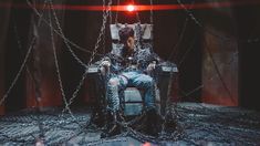 a man sitting in a chair with chains on the floor and lights shining behind him