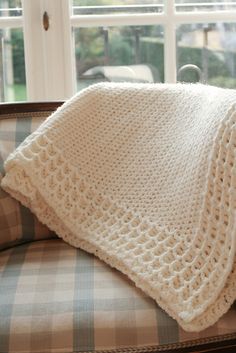 a white crocheted blanket sitting on top of a couch next to a window