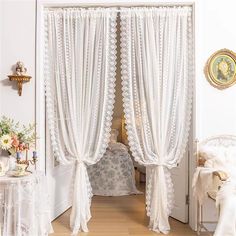 an open door with white curtains and lace on the curtain, in front of a bed