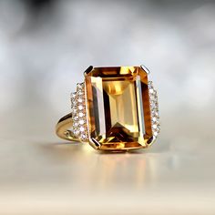 This ring features an 11.35 carat emerald-cut, prong-set natural citrine. Flanking the center stone are two steps of round brilliant cut diamonds set on the shoulders. Adorning the under-gallery is intricate openwork. This ring is handcrafted in 18k yellow gold.
The measurements of the center stone are approximately 16.00mm x 12.06mm x 7.80mm.
This ring can be resized to any finger size at no additional cost.
If you have any questions regarding the Springs Ring, please feel free to contact us. Citrine Engagement Ring, Citrine Ring Engagement, Estate Diamond Jewelry, Emerald Cut Engagement, Elegant Engagement Rings, Emerald Engagement Ring Cut, Yellow Gold Engagement, Citrine Ring, 18k Yellow Gold Ring