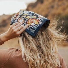 a woman with long blonde hair wearing a bandana on top of her head in the desert