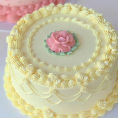 there is a white cake with pink frosting on the top, and a rose decoration on the bottom