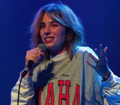 a woman holding a microphone in her right hand and wearing a sweatshirt with the letters aha on it