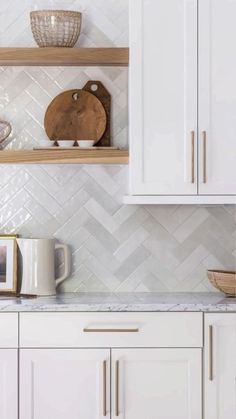 a kitchen with white cupboards and shelves filled with dishes on top of them, next to a wooden cutting board