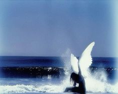 a woman sitting on top of a surfboard in the ocean with an angel wings