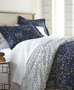 a bed with blue and white comforters on top of it next to a night stand