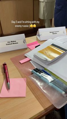 some papers and pens on a table with people in the backgrouf room