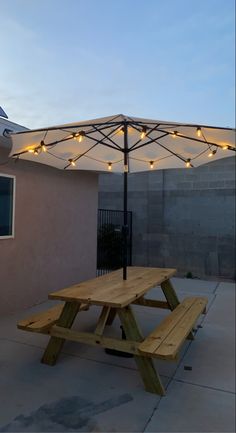 a wooden picnic table under an umbrella with string lights on it outside at dusk in the backyard