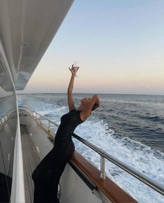 a woman holding up a paper boat in the air while standing on a boat's deck