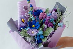 a hand holding a purple paper bouquet with crocheted flowers and leaves on it