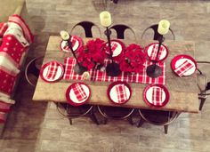 a dining room table set with red and white plaid placemats, candles and flowers