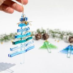 a hand holding a glass ornament in the shape of a christmas tree with blue and green ornaments