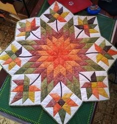 a quilted table topper with an orange and green star design on the center