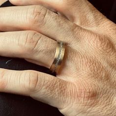 a person's hand with a wedding ring on top of their left hand, resting against a black surface