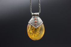 A very unique Hand made Silver Pendant with a replica Amber. Amber is used by Tibetans for centuries. High-quality amber is rare and expensive. The replica is commonly used with Silver as jewelry. In this piece, amber is decorated beautifully with carved silver that has an Auspicious symbol conch shell, flora pattern and coral cabs. Wt: 26g Origin- Nepal 20th c Handmade Amber Necklace For Collectors, Traditional Amber Oval Jewelry, Vintage Carved Amber Jewelry, Vintage Amber Carved Jewelry, Traditional Oval Amber Jewelry, Antique Engraved Amber Jewelry, Collectible Bohemian Amber Jewelry, Traditional Amber Jewelry With Carved Details, Handmade Antique Amber Jewelry