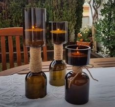 three bottles with candles in them sitting on a table outside next to a candle holder