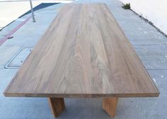 a wooden table sitting on top of a sidewalk next to a parking lot with no people