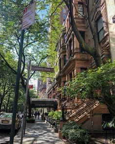 an apartment building on the corner of a city street with trees and people walking down the sidewalk