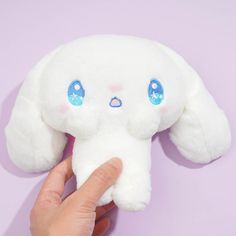 a hand holding a white stuffed animal with blue eyes