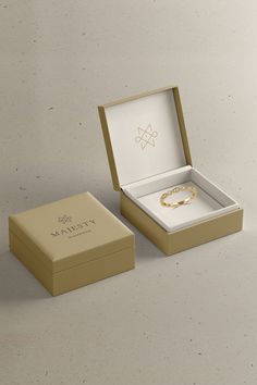 an open box with a gold ring inside on a white surface, next to it's lid