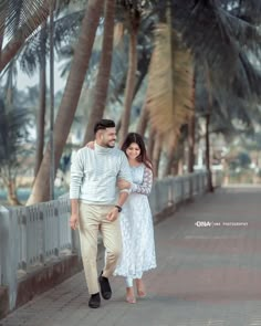 a man and woman walking down a sidewalk next to palm trees in front of them