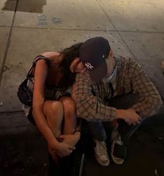 a man and woman sitting next to each other on the sidewalk with their arms around each other