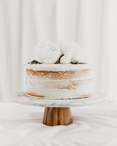 a cake with white frosting and two flowers on top sitting on a wooden stand