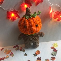 a crocheted stuffed animal with a pumpkin on it's head surrounded by fall leaves