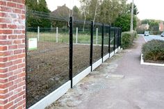 a black fence is next to a brick wall and grass in front of the fence