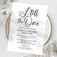 a white wedding card with the words still the one on it next to a plate