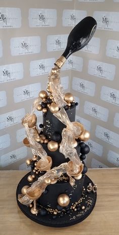 a black and gold christmas tree with lots of ornaments on it's base, in front of a wall