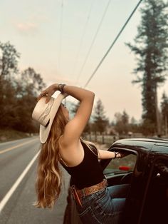 a woman leaning out the window of a car with her cowboy hat hanging over her head