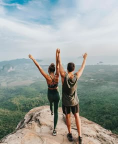 two people standing on top of a mountain with their arms in the air and hands up