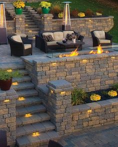 an outdoor fire pit surrounded by stone steps and seating area with yellow flowers on the side