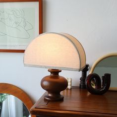 a lamp sitting on top of a wooden dresser next to a mirror and framed artwork