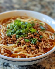 a bowl of noodles with meat and green onions