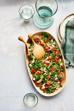 a wooden spoon sitting on top of a pan filled with salad next to plates and glasses