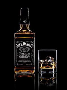 a bottle of jack daniels whiskey next to a glass with ice cubes in it