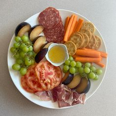 a white plate topped with lots of different types of food next to crackers and grapes