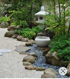 a garden with rocks, gravel and a water feature in the center is surrounded by greenery