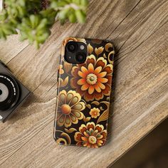 an iphone case with flowers on it sitting on a wooden table next to a camera