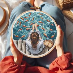 a woman is holding up a cross - stitch pattern with goldfish in the water