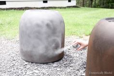 a person holding a can next to two large metal trash cans on the ground in front of a house