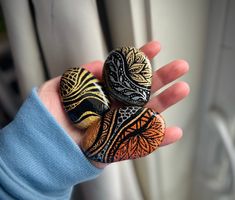 two rocks are sitting on someone's hand, one is decorated with an intricate design