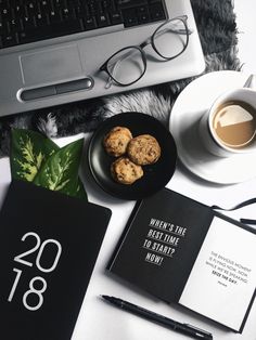 a desk with a laptop, notebook and some cookies on it next to a cup of coffee