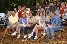 a group of people sitting next to each other on top of a bench in front of a crowd