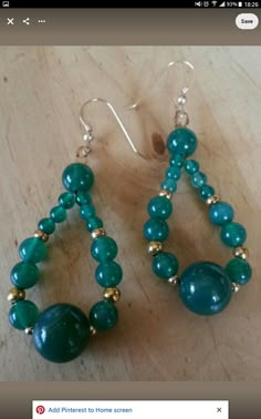 two pairs of earrings with green beads and gold accents on a wooden surface, ready to be worn