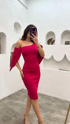 a woman in a red dress taking a selfie with her cell phone while standing next to a white wall