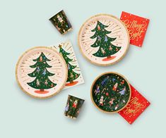 three plates with christmas trees on them and napkins next to each other in front of a blue background