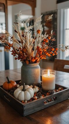 a candle and some flowers in a vase on a tray with other autumn decorations around it